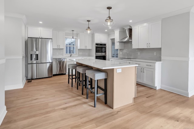 kitchen featuring white cabinetry, hanging light fixtures, wall chimney range hood, a kitchen island, and appliances with stainless steel finishes