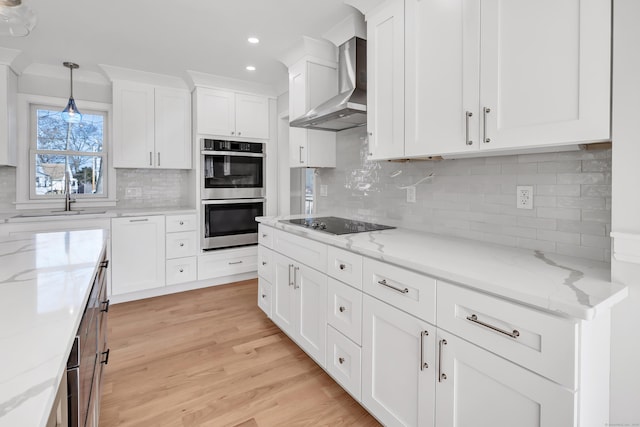 kitchen with tasteful backsplash, wall chimney exhaust hood, double oven, white cabinets, and hanging light fixtures