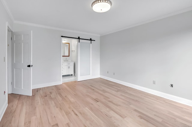 unfurnished bedroom with ensuite bathroom, crown molding, sink, a barn door, and light hardwood / wood-style floors