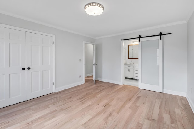 unfurnished bedroom featuring a barn door, a closet, crown molding, and connected bathroom