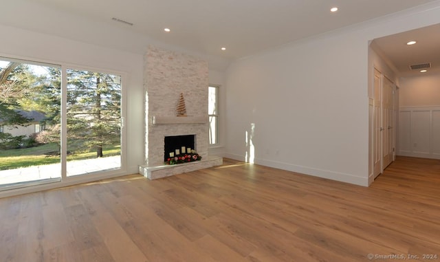 unfurnished living room with a stone fireplace, a wealth of natural light, ornamental molding, and light wood-type flooring