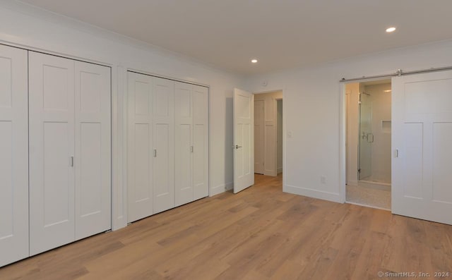 unfurnished bedroom featuring a barn door, light hardwood / wood-style floors, and multiple closets