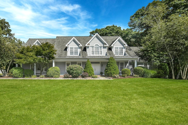 cape cod-style house featuring a shingled roof and a front yard