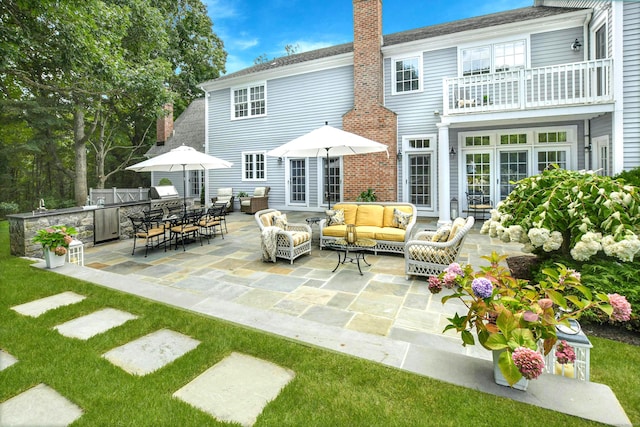 back of property with a balcony, a chimney, french doors, a patio area, and an outdoor living space