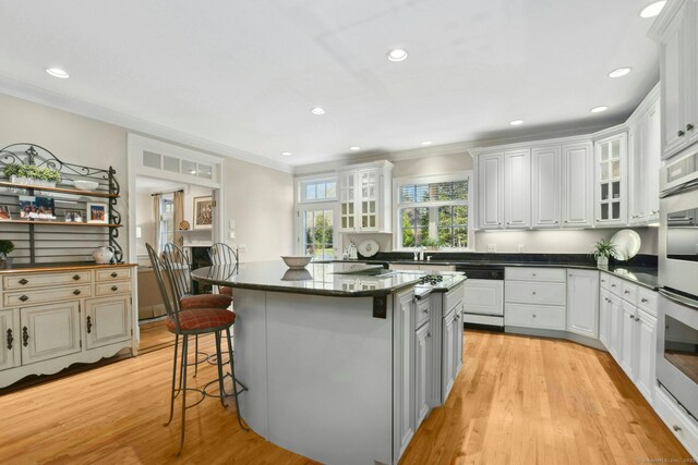 kitchen featuring a center island, a breakfast bar area, light wood-style floors, glass insert cabinets, and stainless steel double oven