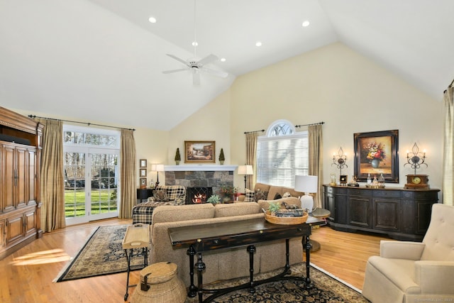 living room featuring ceiling fan, a stone fireplace, light wood-type flooring, high vaulted ceiling, and recessed lighting