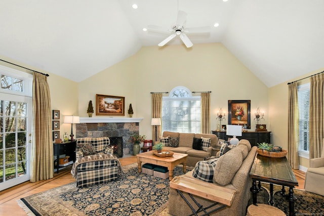 living area with light wood-style flooring, high vaulted ceiling, a stone fireplace, and ceiling fan