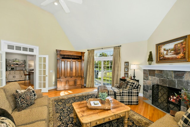 living area featuring light wood finished floors, baseboards, a stone fireplace, french doors, and high vaulted ceiling