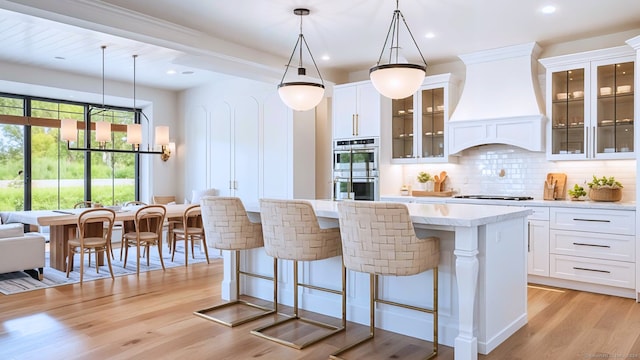 kitchen featuring a kitchen island, double oven, white cabinetry, hanging light fixtures, and custom range hood