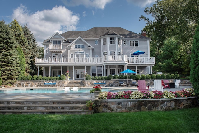 back of property with a patio area, an outdoor pool, french doors, and a balcony