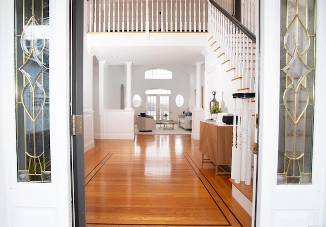 entryway featuring decorative columns, french doors, light wood-type flooring, and a towering ceiling