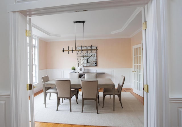 dining room with a wainscoted wall, wood finished floors, a decorative wall, and ornamental molding