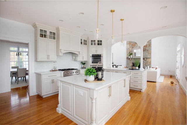 kitchen featuring a center island with sink, arched walkways, stainless steel appliances, light countertops, and light wood-style floors