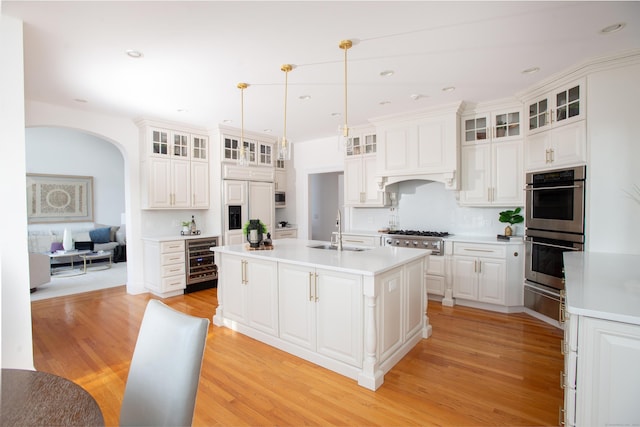 kitchen with beverage cooler, a center island with sink, light wood finished floors, a sink, and stainless steel appliances