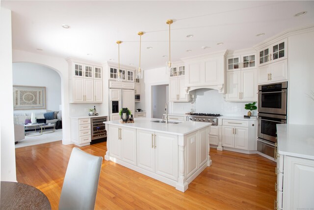 266 Great Plain Rd, Danbury, CT 06811 - kitchen with appliances with stainless steel finishes, beverage cooler, arched walkways, a kitchen island with sink, and light wood-style floors