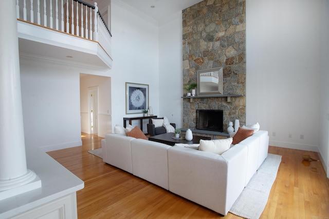 living area with baseboards, ornamental molding, a stone fireplace, light wood-style flooring, and a towering ceiling