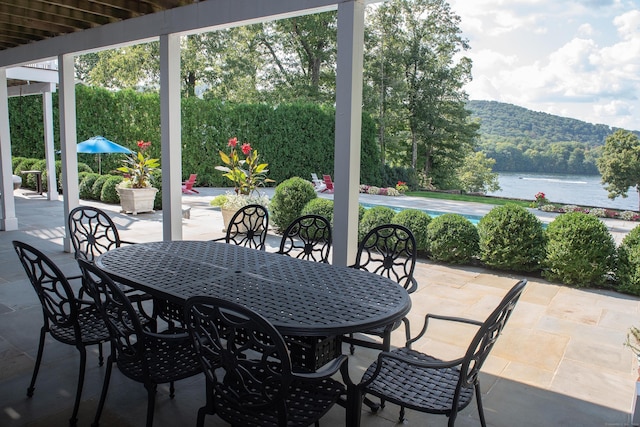 view of patio featuring outdoor dining space, a wooded view, and a water view