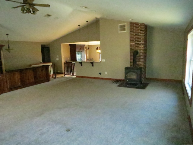 unfurnished living room with ceiling fan, vaulted ceiling, and a wood stove