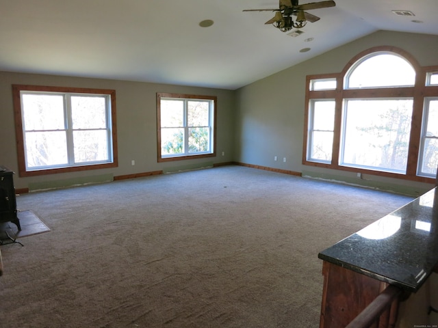 carpeted empty room featuring ceiling fan, lofted ceiling, and a wood stove