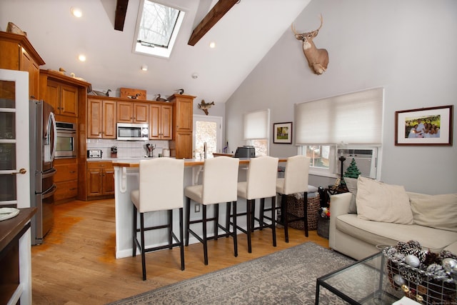 kitchen featuring a skylight, a kitchen breakfast bar, tasteful backsplash, beamed ceiling, and appliances with stainless steel finishes