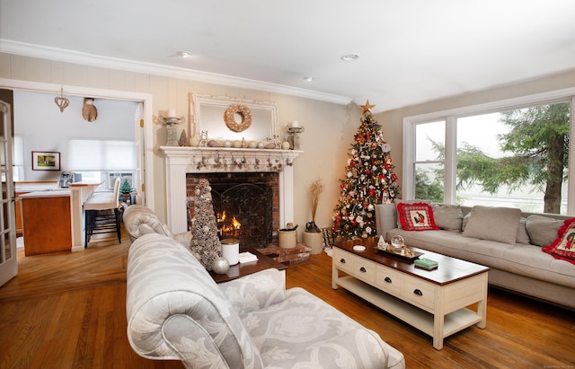 living room with hardwood / wood-style floors, ornamental molding, and a brick fireplace