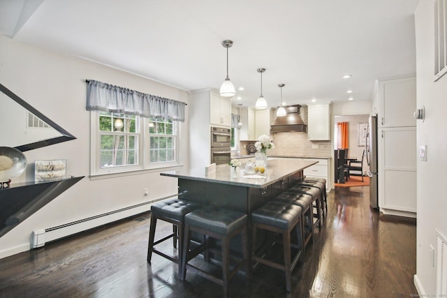 kitchen with baseboard heating, white cabinetry, premium range hood, a kitchen bar, and decorative light fixtures