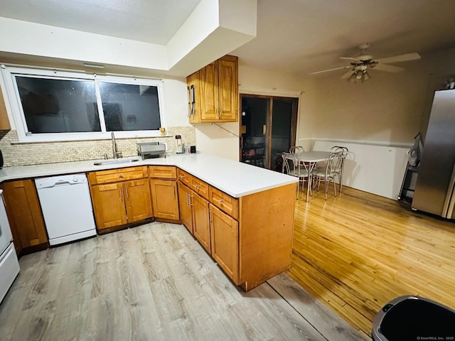 kitchen featuring kitchen peninsula, light wood-type flooring, tasteful backsplash, white dishwasher, and sink