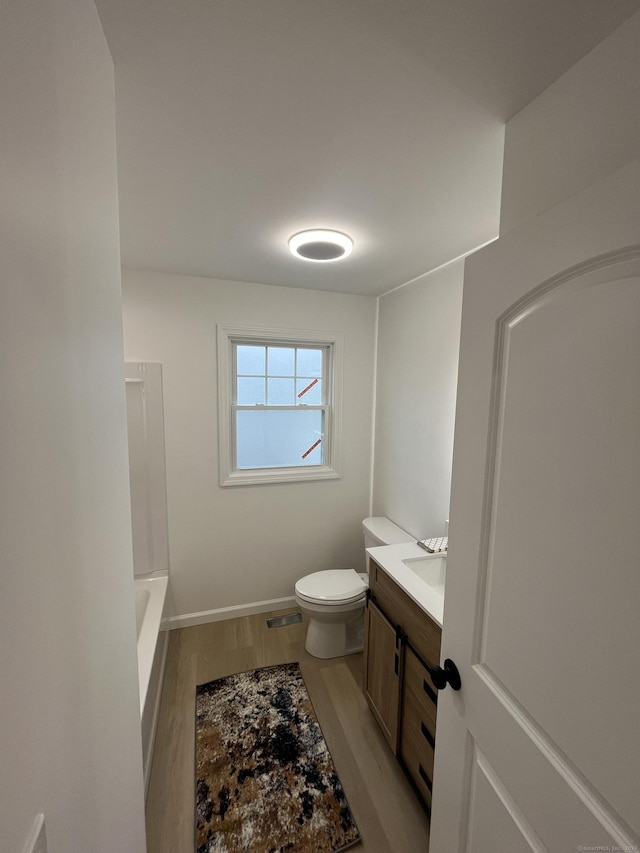 bathroom featuring a washtub, wood-type flooring, vanity, and toilet