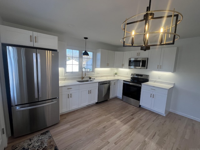 kitchen featuring appliances with stainless steel finishes, sink, decorative light fixtures, light hardwood / wood-style flooring, and white cabinetry