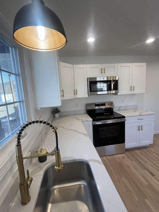 kitchen with white cabinets, sink, appliances with stainless steel finishes, light hardwood / wood-style floors, and light stone counters