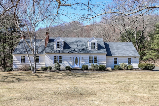 new england style home with a chimney, a front yard, and a shingled roof