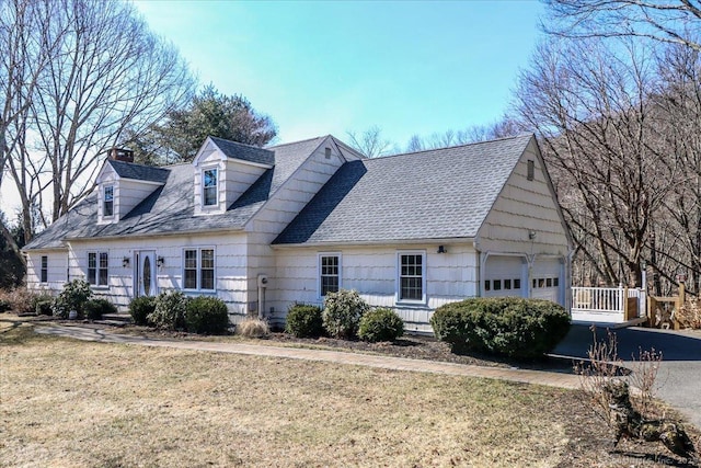 cape cod home featuring a front yard, a chimney, an attached garage, and a shingled roof