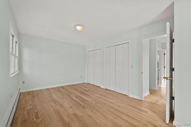 unfurnished bedroom with two closets, light wood-type flooring, and a baseboard heating unit