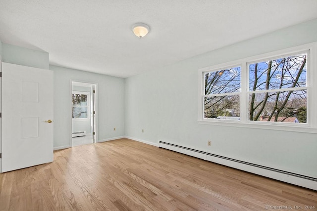 unfurnished bedroom featuring a baseboard heating unit and light hardwood / wood-style floors