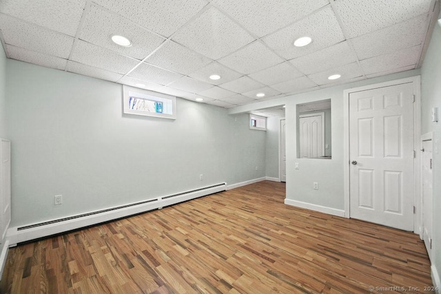 basement with wood-type flooring, a paneled ceiling, and baseboard heating