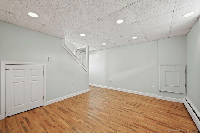 basement featuring a drop ceiling, light hardwood / wood-style flooring, and baseboard heating