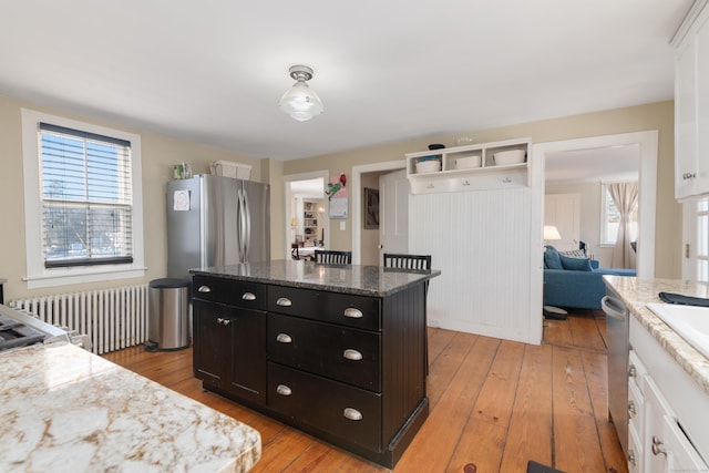 kitchen featuring a center island, white cabinets, light wood-type flooring, light stone counters, and radiator heating unit