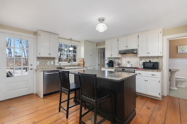 kitchen with white cabinetry, stainless steel dishwasher, dark stone counters, and light hardwood / wood-style floors