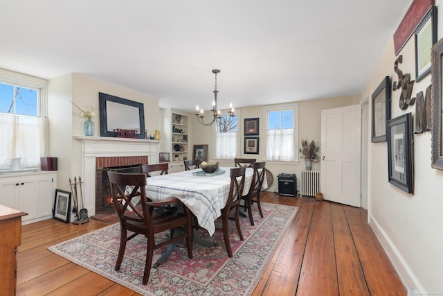 dining space with a brick fireplace, radiator heating unit, a chandelier, and light wood-type flooring