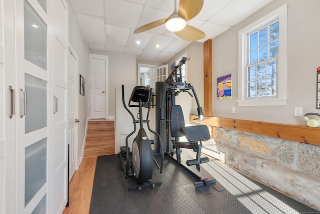 exercise room featuring a paneled ceiling, ceiling fan, and wood-type flooring