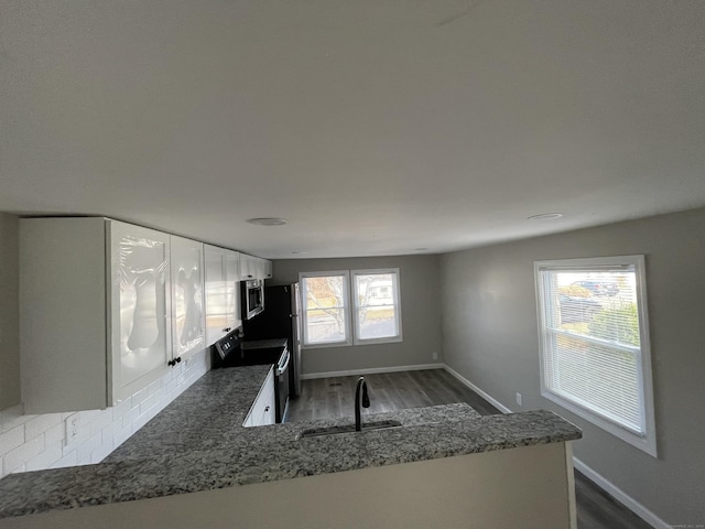 kitchen featuring dark wood-type flooring, kitchen peninsula, sink, appliances with stainless steel finishes, and white cabinetry