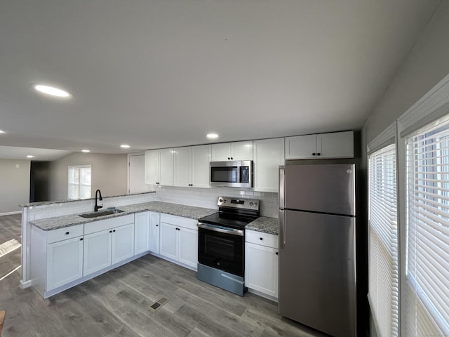 kitchen with appliances with stainless steel finishes, a wealth of natural light, sink, white cabinets, and light hardwood / wood-style floors