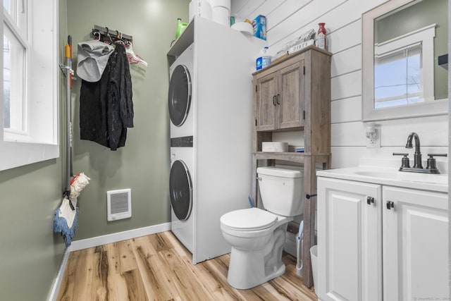 clothes washing area with stacked washer and dryer, light hardwood / wood-style flooring, plenty of natural light, and sink