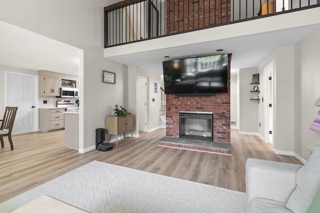 living room featuring light wood-type flooring, a fireplace, and a high ceiling