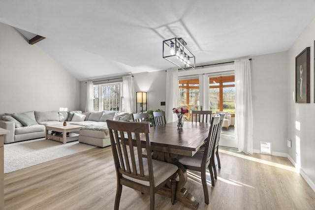 dining room with light hardwood / wood-style floors, vaulted ceiling, a healthy amount of sunlight, and a notable chandelier