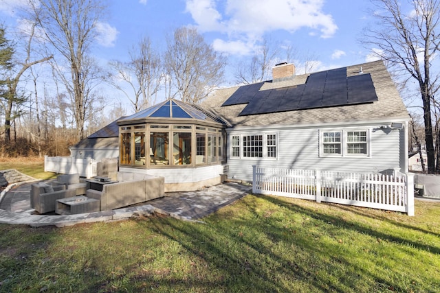 rear view of house with a sunroom, solar panels, a patio area, and a lawn