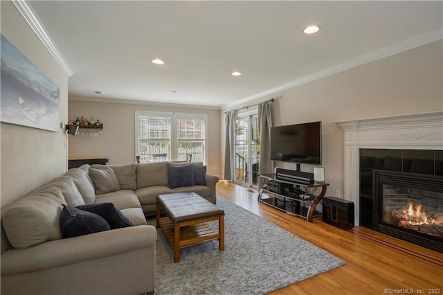 living room featuring wood-type flooring, crown molding, and a tiled fireplace