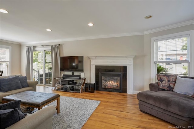 living room with a tile fireplace, crown molding, and light wood-type flooring