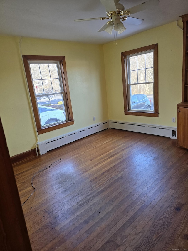 spare room with ceiling fan, a healthy amount of sunlight, dark wood-type flooring, and a baseboard heating unit