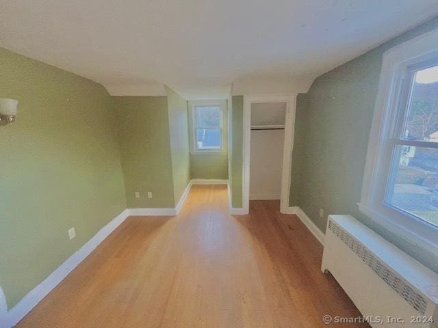 empty room with radiator heating unit, light wood-type flooring, and vaulted ceiling